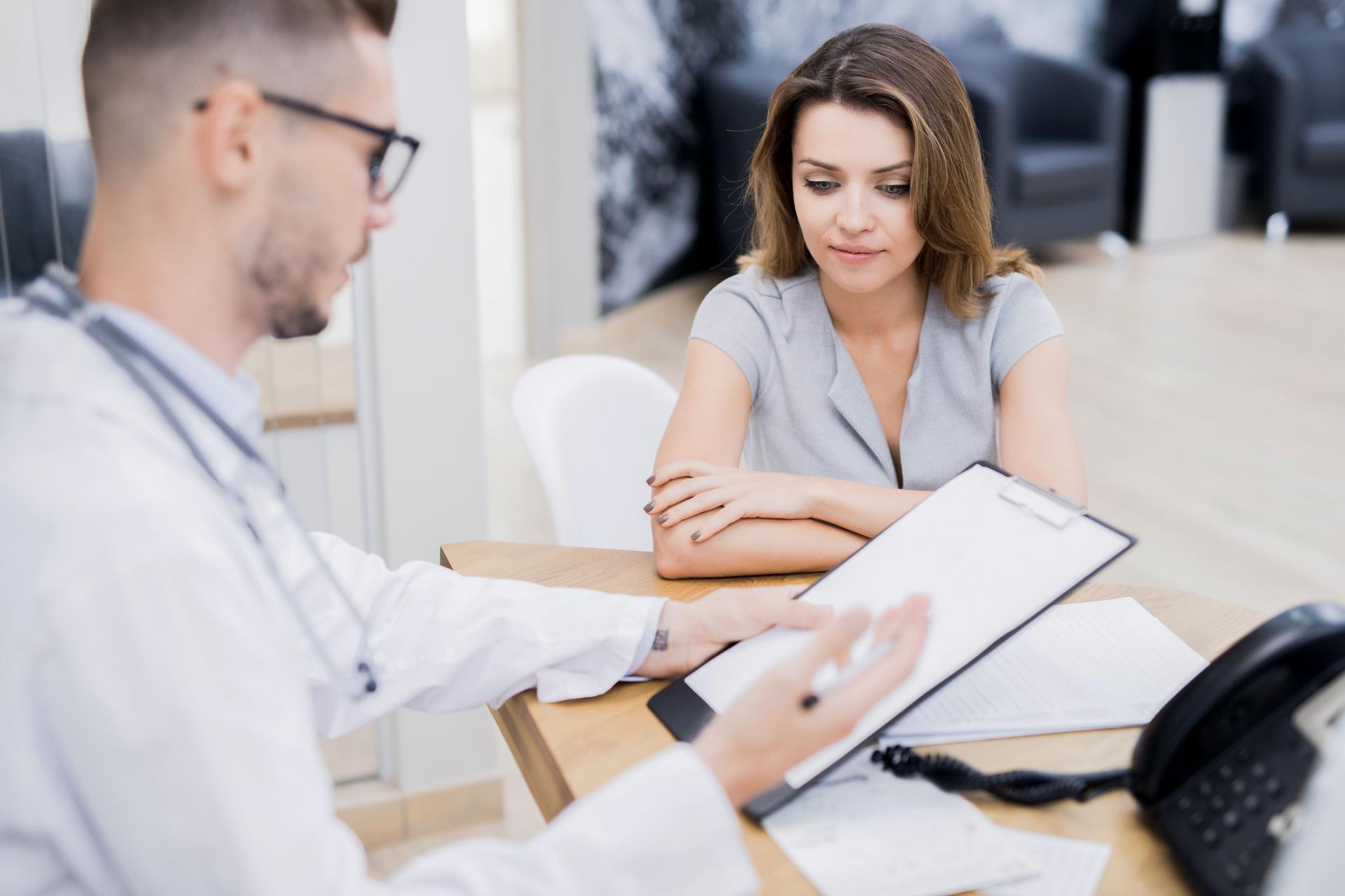 Qualifizierter junger Arzt Betrieb Klemmbrett mit Gesundheitskarte und erklären diagnostizieren Patienten während ärztliche Beratung in Klinik